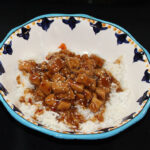 A dish of Bourbon Chicken served over a bed of white rice.