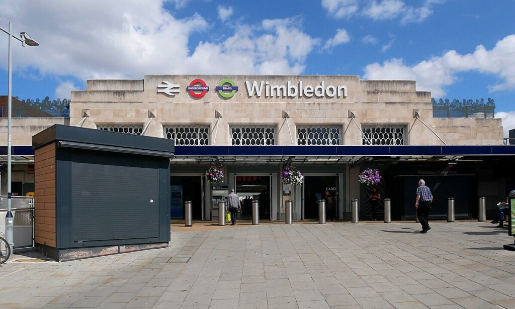 Main entrance to Wimbledon Station with signage and people walking by.