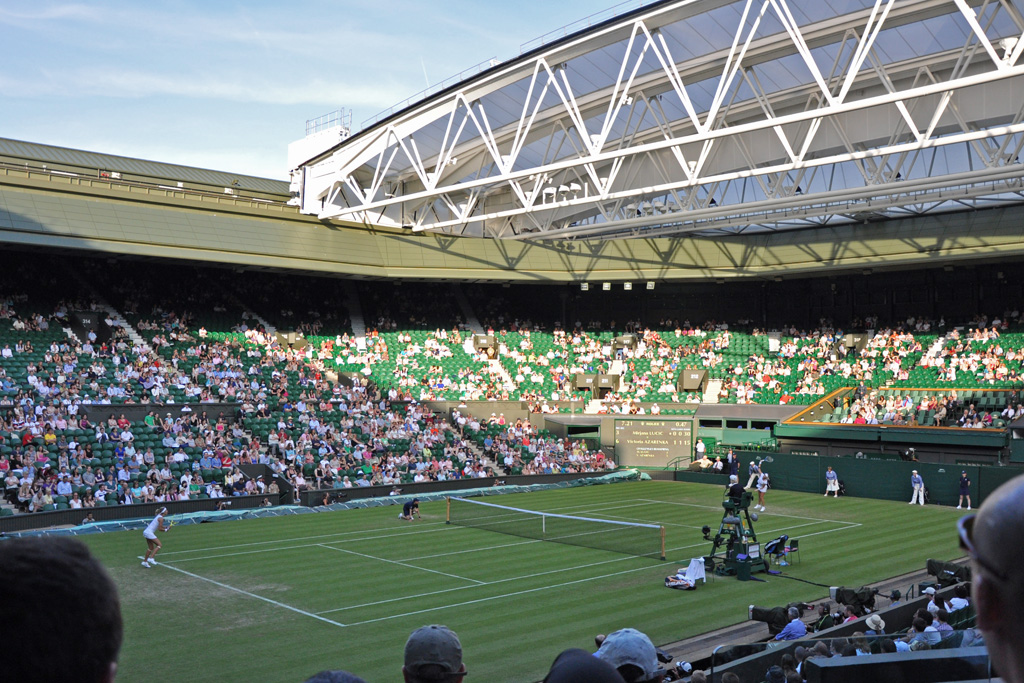 Wimbledon Centre Court during a match, with the retractable roof partially open and spectators in the stands.